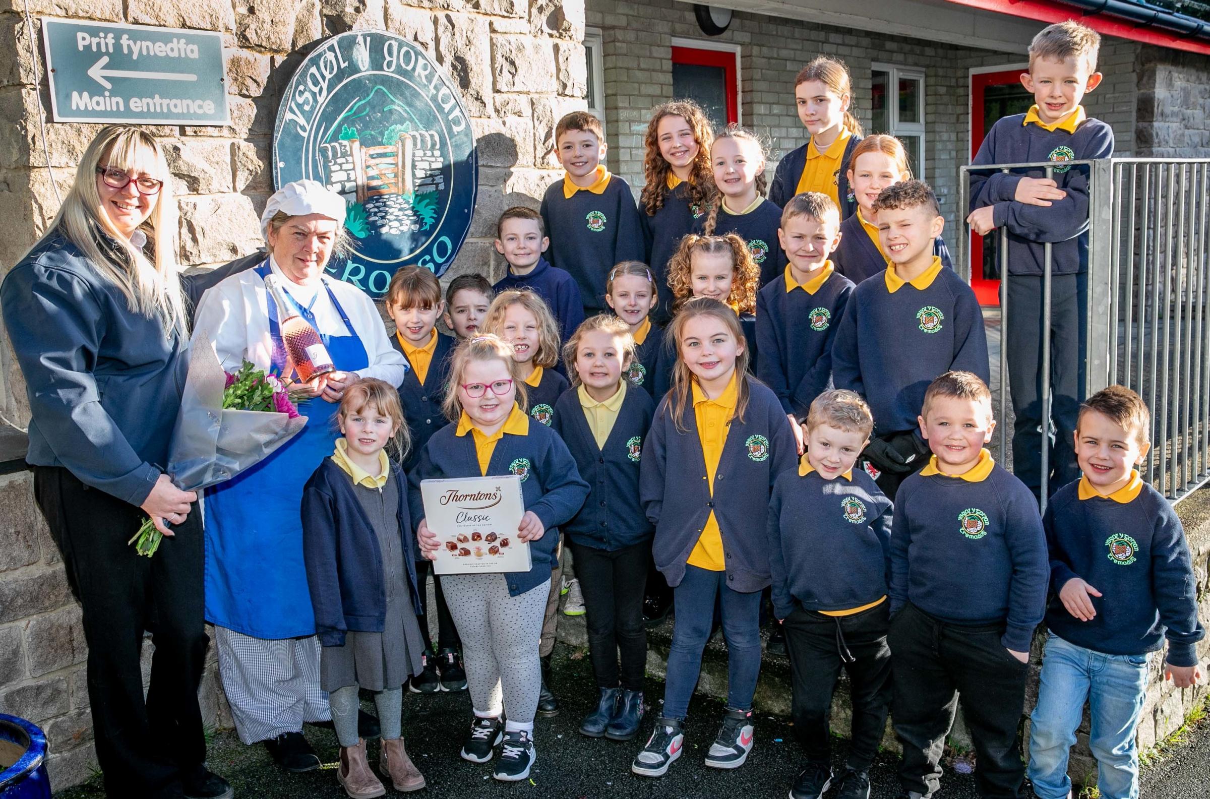 Watched by pupils of Ysgol Y Gorlas, Tremadog, school cookRhian Parry, retiring after 35 years, is presented with flowers, chocolatesand bubbly by Ursula Scurrah-Price, of Harlech Foodservice, a former pupilwho is now in charge of food deliveries to