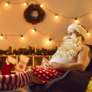 Santa watching tv surrounded by Christmas decorations. Credit: Canva