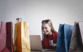 A woman shopping online surrounded by shopping bags. Credit: Canva